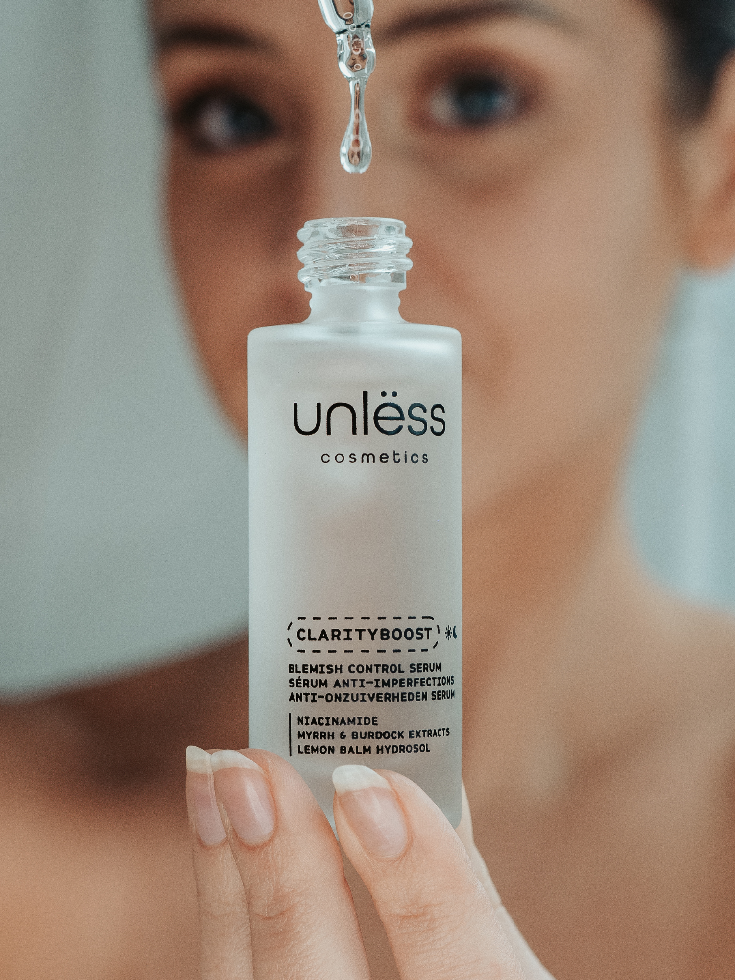 Goutte du sérum Clarityboost tombant d’une pipette dans son flacon, avec une utilisatrice floutée en arrière-plan.