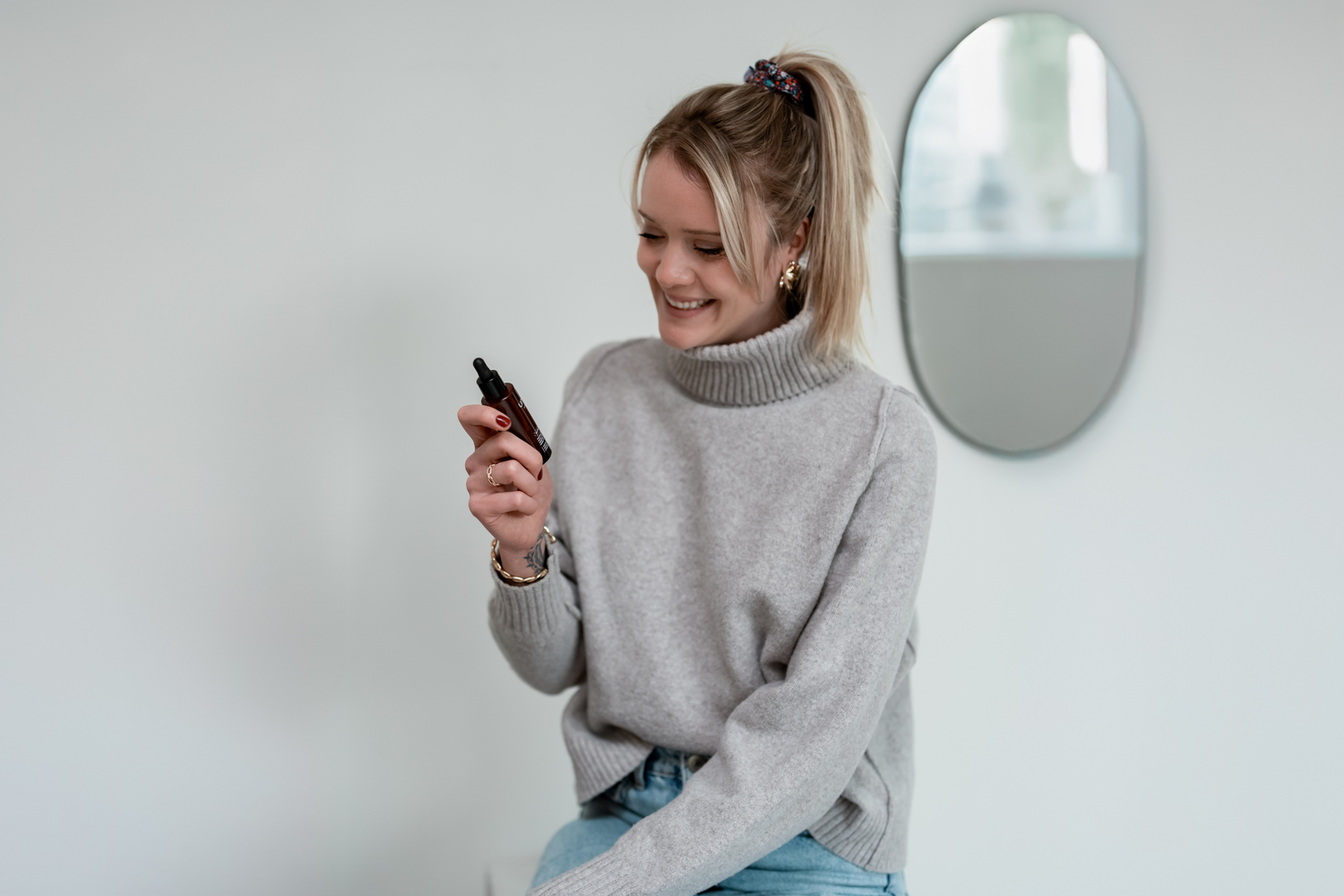 Femme souriante tenant en main et regardant l’huile sèche restructurante Nutrirepair d’Unlëss Cosmetics.