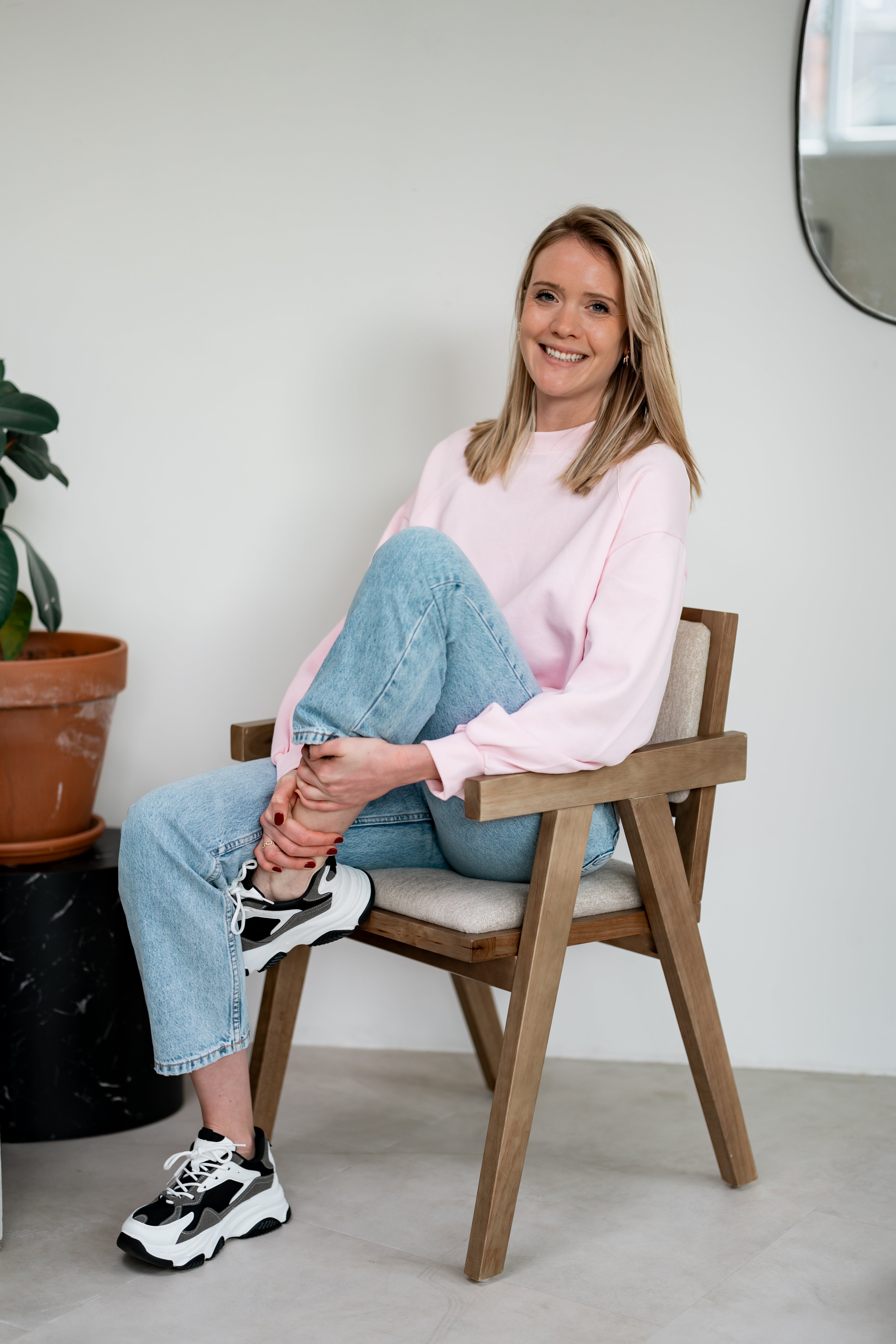 Femme souriante assise sur une chaise devant un fond neutre.