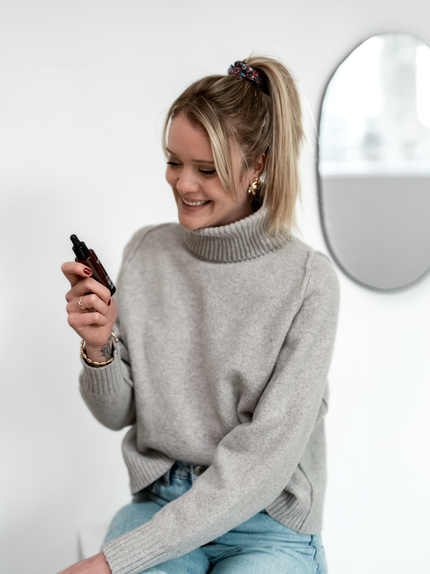 Femme souriante tenant en main et regardant l’huile sèche restructurante Nutrirepair d’Unlëss Cosmetics.