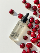 Sérum Oxishield d’Unlëss Cosmetics posé sur un fond texturé blanc, entouré de canneberges rouges avec une ombre marquée du flacon.